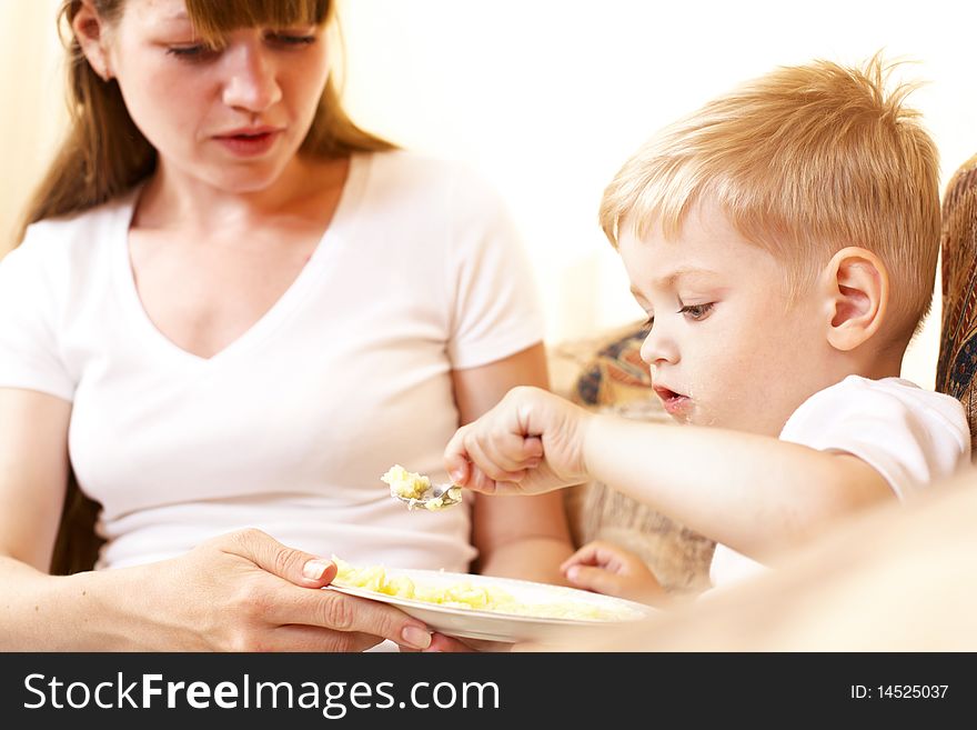 Mother feeding her little son at home; shallow DOF, focus on boys eyes. Mother feeding her little son at home; shallow DOF, focus on boys eyes