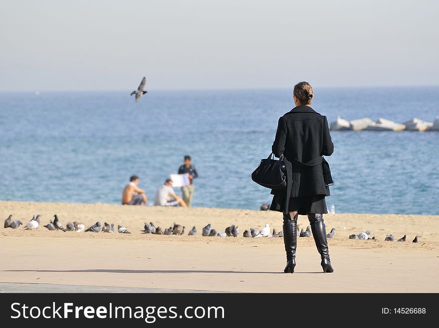 Woman looking for the sea at the Barceloneta sea beach in Barcelona, Spain; focus on the women' figure, background is blurred by lens defocusing. Woman looking for the sea at the Barceloneta sea beach in Barcelona, Spain; focus on the women' figure, background is blurred by lens defocusing