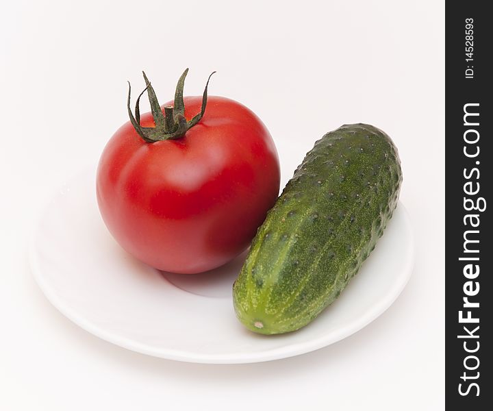 Green cucumber and red tomato on white saucer. Green cucumber and red tomato on white saucer