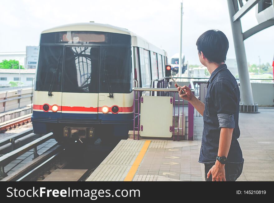 Asian man passenger using smartphone and looking BTS in train station ,skytrain wait on BTS Skytrain station