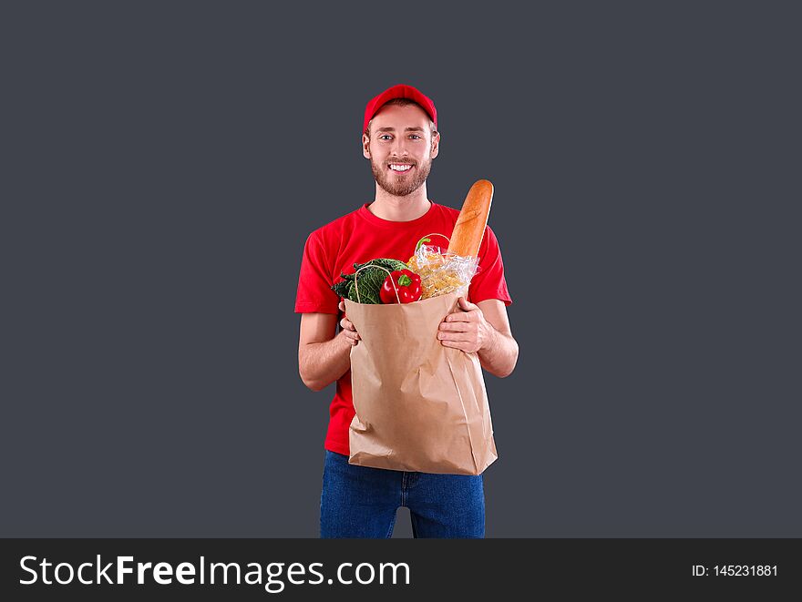 Delivery man holding paper bag with food products on dark background