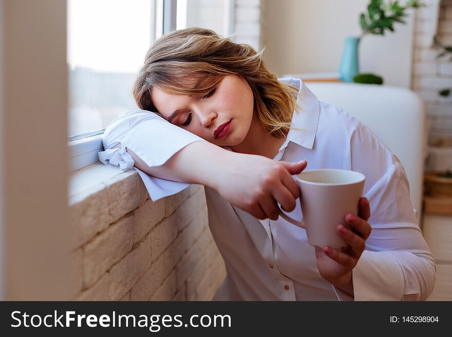 Nice tired woman falling asleep with a cup of tea