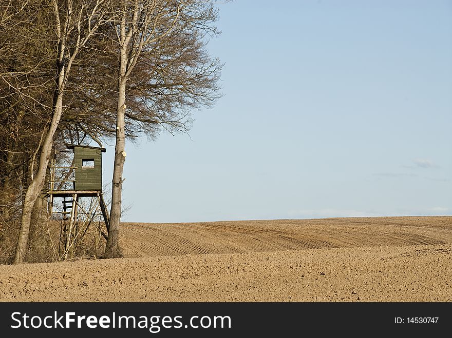 A deerstand at the edge of a plowed acre