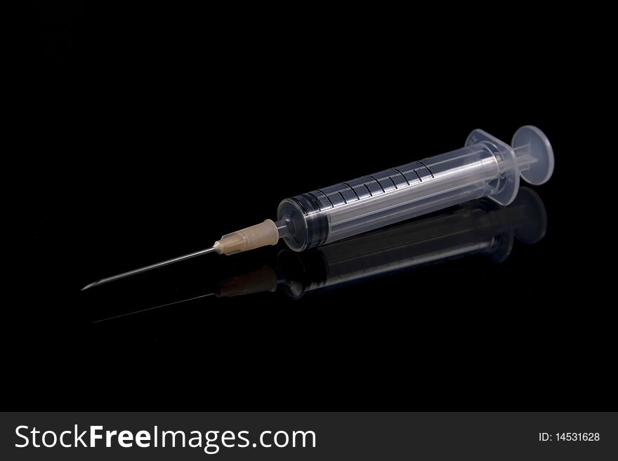 A syringe with hypodermic needle on a reflective black background.