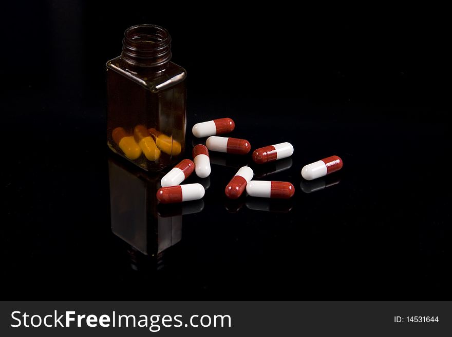 Medical pills and a prescription bottle on a reflective black background