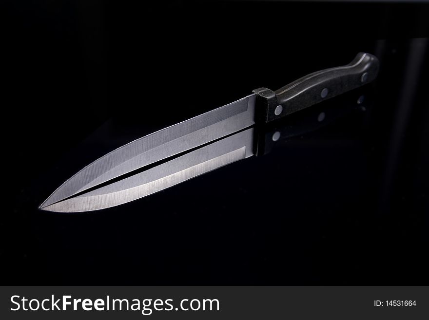 A single kitchen knife on a black reflective background