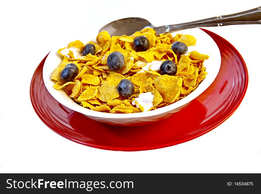 White bowl of corn flakes with fresh blueberries on a red plate, on an isolated white background.