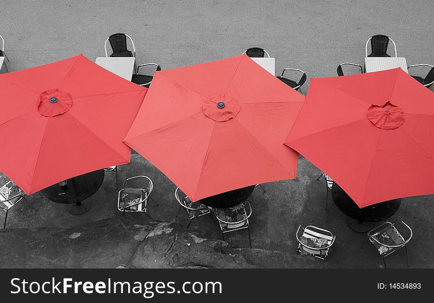 Large red umbrellas in street cafe viewed from above.