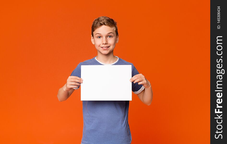 Friendly teen boy holding white blank placard with empty space for your text or product, orange background. Friendly teen boy holding white blank placard with empty space for your text or product, orange background