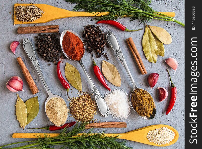 Different spices in wooden and metall spoons on grey background. Bay leaf. Garlic. Fennel. Mustard seeds. Zira. Red pepper. Ginger root. Black pepper. Carnation. Pepper pods. Cinnamon. Salt. Sesame seed. Different spices in wooden and metall spoons on grey background. Bay leaf. Garlic. Fennel. Mustard seeds. Zira. Red pepper. Ginger root. Black pepper. Carnation. Pepper pods. Cinnamon. Salt. Sesame seed.