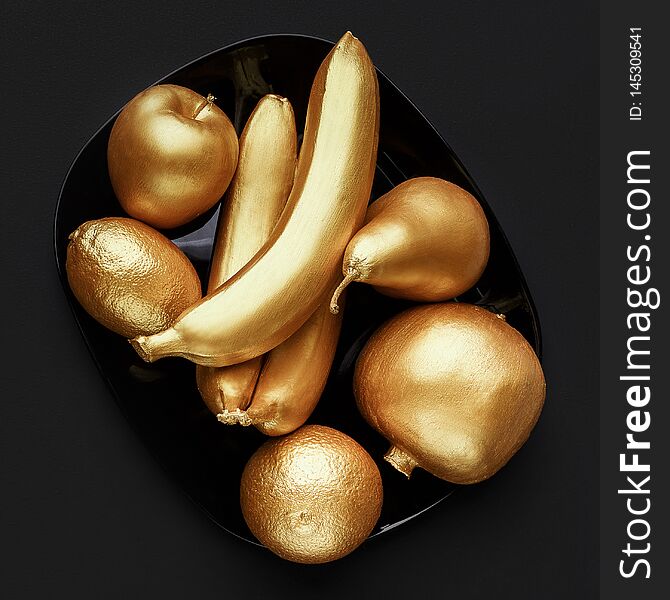 Fruits in golden glaze on plate over black background, top view.