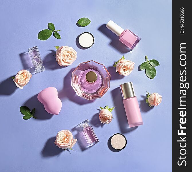 Flat lay composition with bottles of perfume, cosmetics and roses on color background