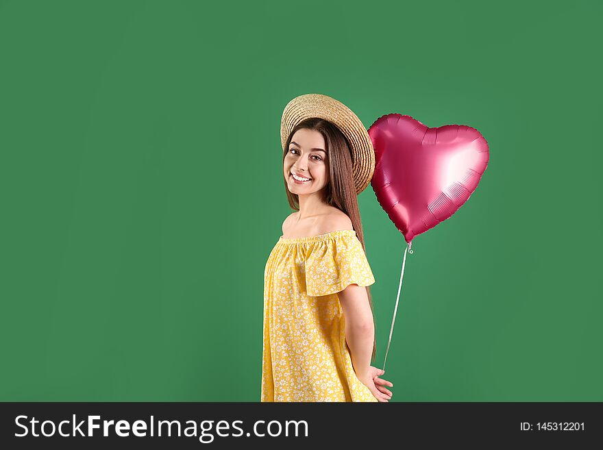 Portrait of young woman with heart shaped balloon on color background