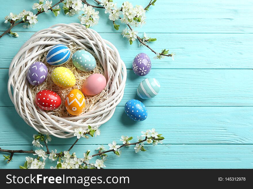 Flat lay composition with painted Easter eggs and blossoming branches on wooden background. Space for text