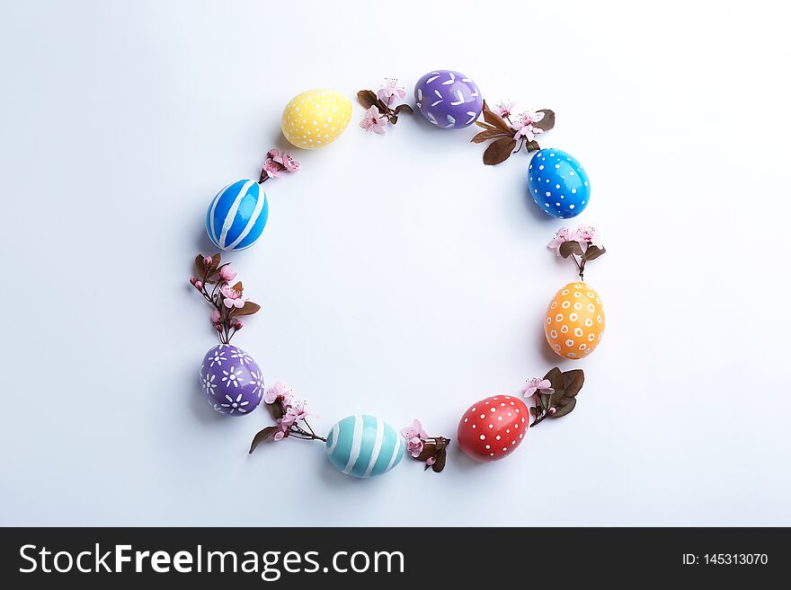 Frame made of painted Easter eggs and blossoming branches on white background, top view.