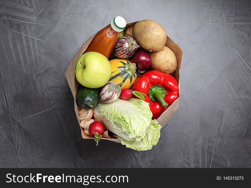 Paper package with fresh vegetables, apple and bottle of juice on dark background, top view