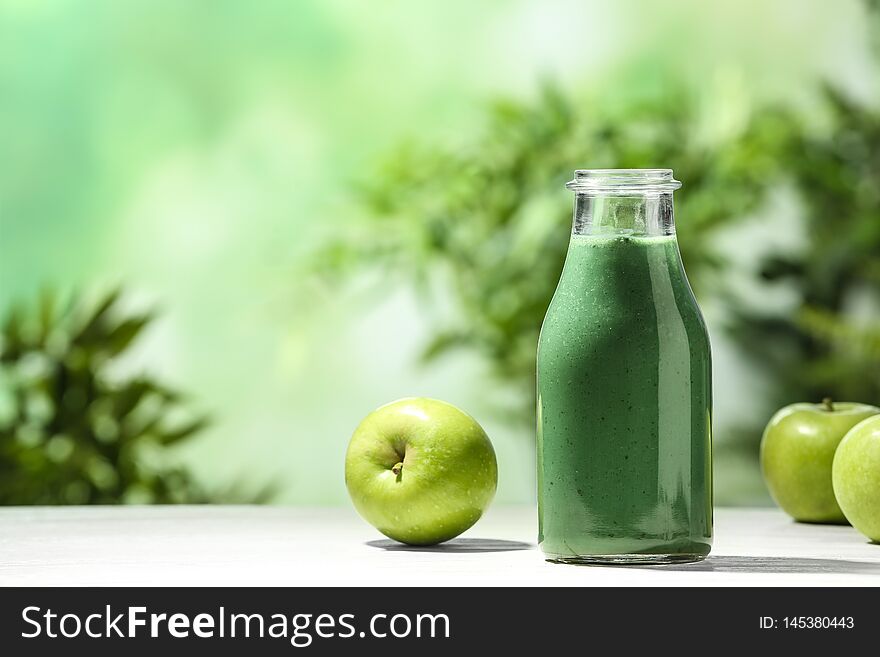 Bottle of spirulina smoothie and apples on table against blurred background. Space for text