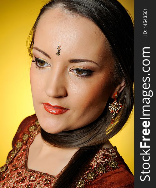 Young beautiful woman in indian traditional jewellary, bindi and sari dress. yellow background. Young beautiful woman in indian traditional jewellary, bindi and sari dress. yellow background