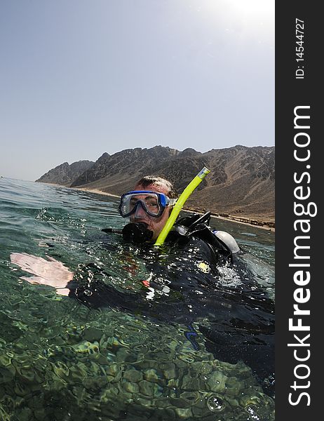 Male scuba diver on surface with mountains behind. Male scuba diver on surface with mountains behind