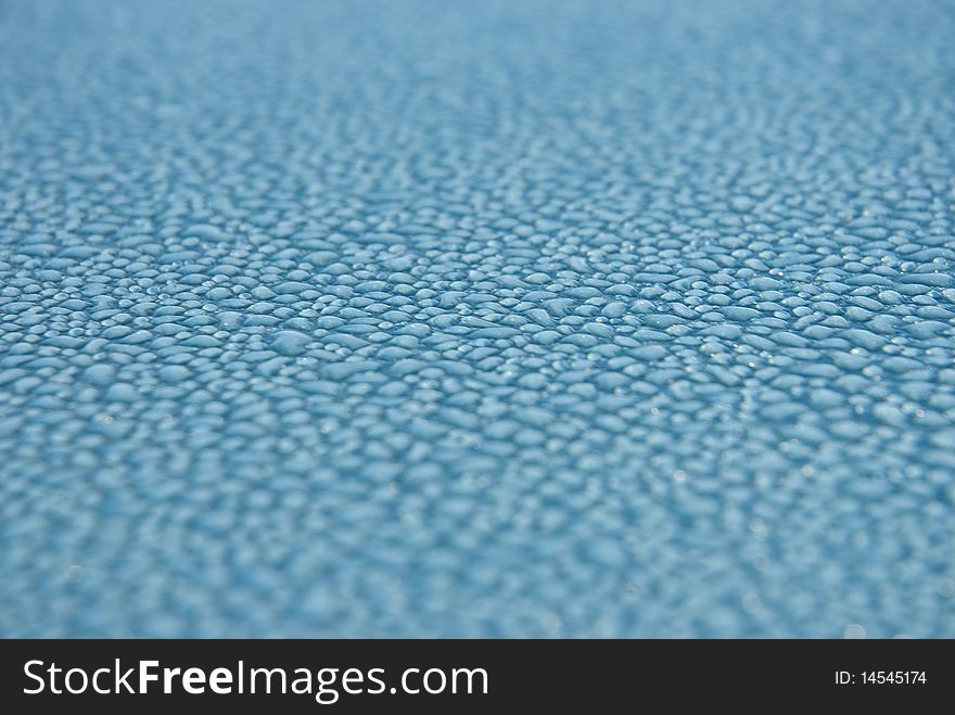 Close-up shot of dew drops on a light blue or turquoise metallic surface, glistening from the light. Close-up shot of dew drops on a light blue or turquoise metallic surface, glistening from the light