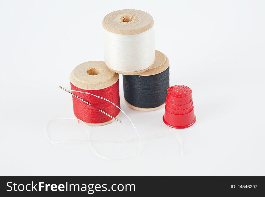 Three reels of cotton with a sewing needle and a thimble isolated on white. Three reels of cotton with a sewing needle and a thimble isolated on white