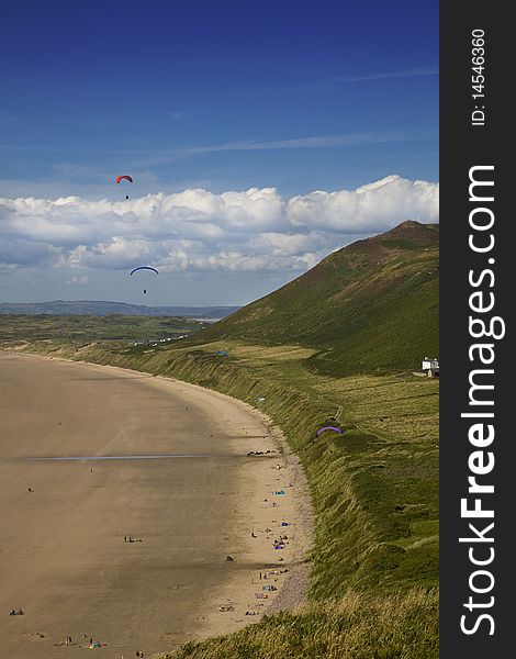 View of Rhossili Bay with hills and cloudy blue sky with parasailors. View of Rhossili Bay with hills and cloudy blue sky with parasailors.