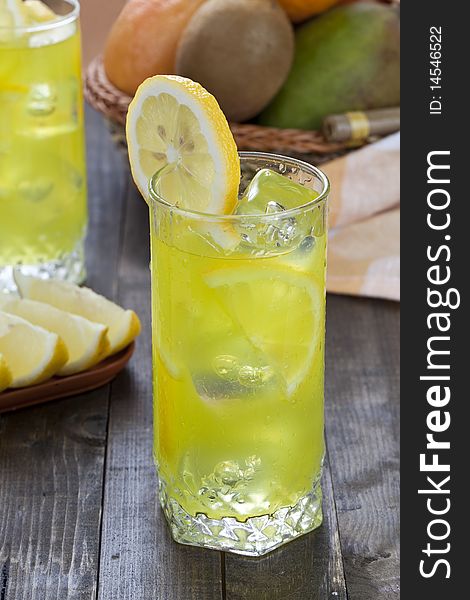 Glass of cold lemon cocktail with ice cubes on wooden table top. Glass of cold lemon cocktail with ice cubes on wooden table top