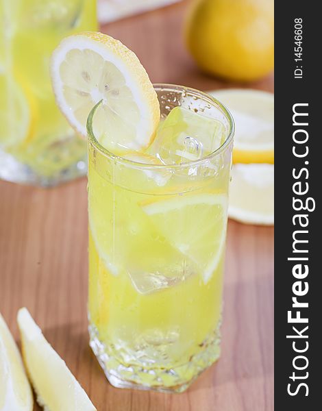 Glass of cold lemon beverage with slices of lemon fruit on wooden table top. Glass of cold lemon beverage with slices of lemon fruit on wooden table top