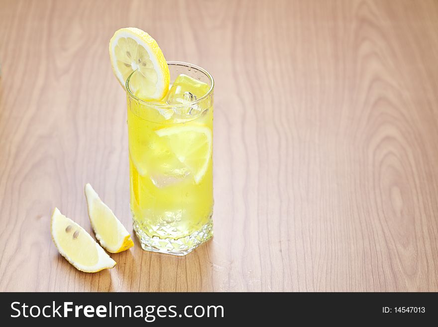 Glass of cold lemon beverage with slices of lemon fruit on wooden table top. Glass of cold lemon beverage with slices of lemon fruit on wooden table top