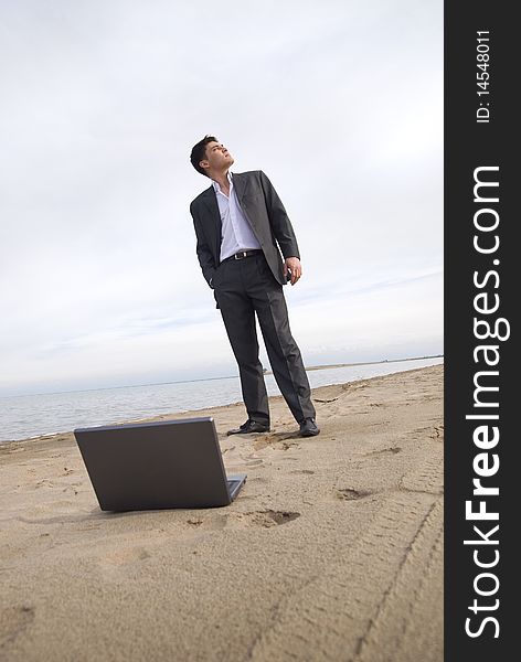 Guy in a suit standing on the beach looking up. before him laptop. Guy in a suit standing on the beach looking up. before him laptop