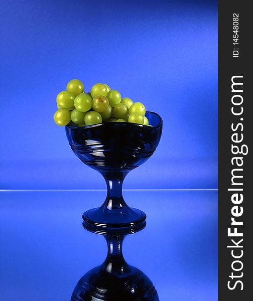 Green grapes in glass bowl isolated on mirrow and blue background