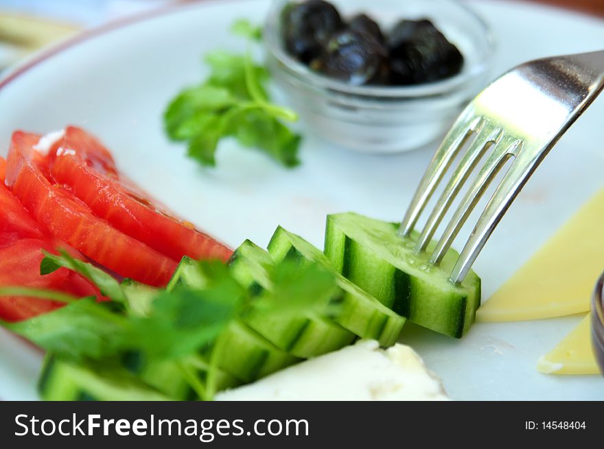 Close of up fork on a plate of a beautiful Turkish breakfast, that can be considered a salad as well. There are tomatoes, cucumbers, olives, and two types of cheese. Close of up fork on a plate of a beautiful Turkish breakfast, that can be considered a salad as well. There are tomatoes, cucumbers, olives, and two types of cheese.