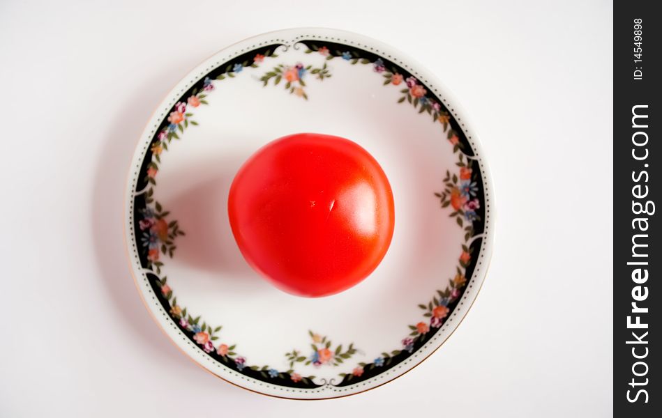 The tomato lies in a saucer on a white background