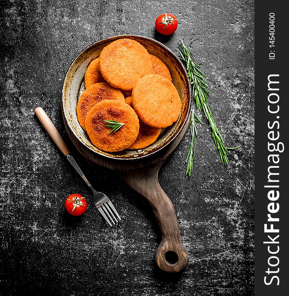 Fish cutlets in pan with fork and rosemary. On black rustic background