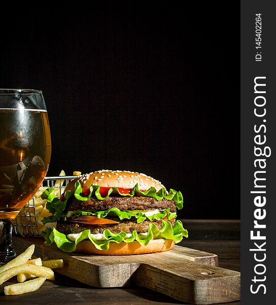 Burger with beer in a glass and fries. On wooden background