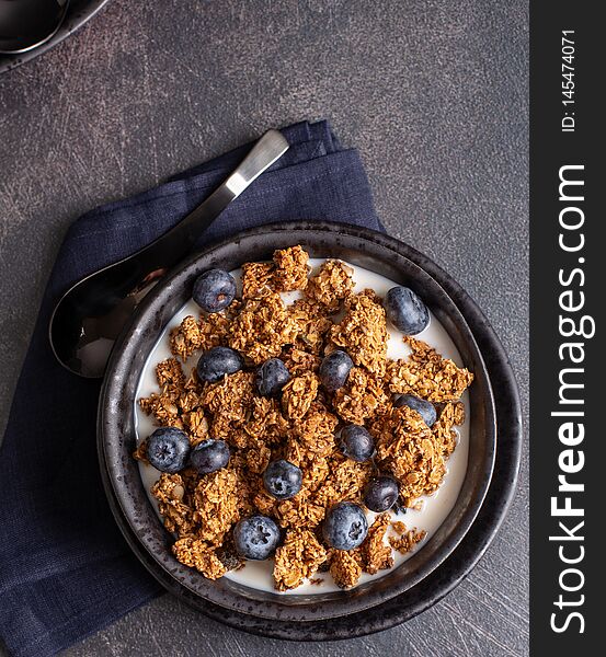 Overhead view of a bowl of granola with fresh blueberries and milk on a dark background. Overhead view of a bowl of granola with fresh blueberries and milk on a dark background