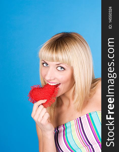 Attractive woman biting a red heart over blue background. Attractive woman biting a red heart over blue background