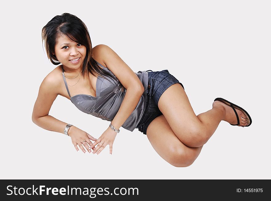 A young pretty Cambodian woman, in shorts and silver gray top, lying on the floor in the studio and looking into the camera, on white background. A young pretty Cambodian woman, in shorts and silver gray top, lying on the floor in the studio and looking into the camera, on white background.