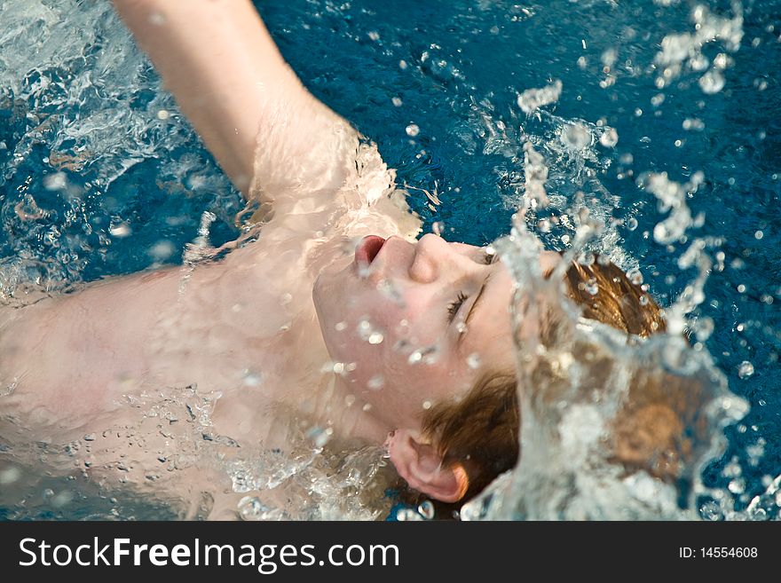 Smiling and happy boy with red hair is swimming and relaxing in a beautiful pool. Smiling and happy boy with red hair is swimming and relaxing in a beautiful pool