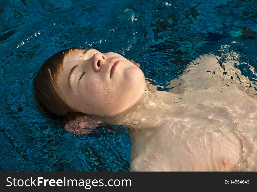 Boy with red hair and closed eyes is swimming and relaxing in a beautiful pool. Boy with red hair and closed eyes is swimming and relaxing in a beautiful pool