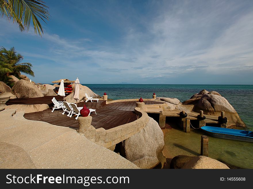 A little private pier of a resort in Koh Tao island, Thailand, near a sundeck on the rocks, with lounge chairs and a hut with canoes for guests. A little private pier of a resort in Koh Tao island, Thailand, near a sundeck on the rocks, with lounge chairs and a hut with canoes for guests.