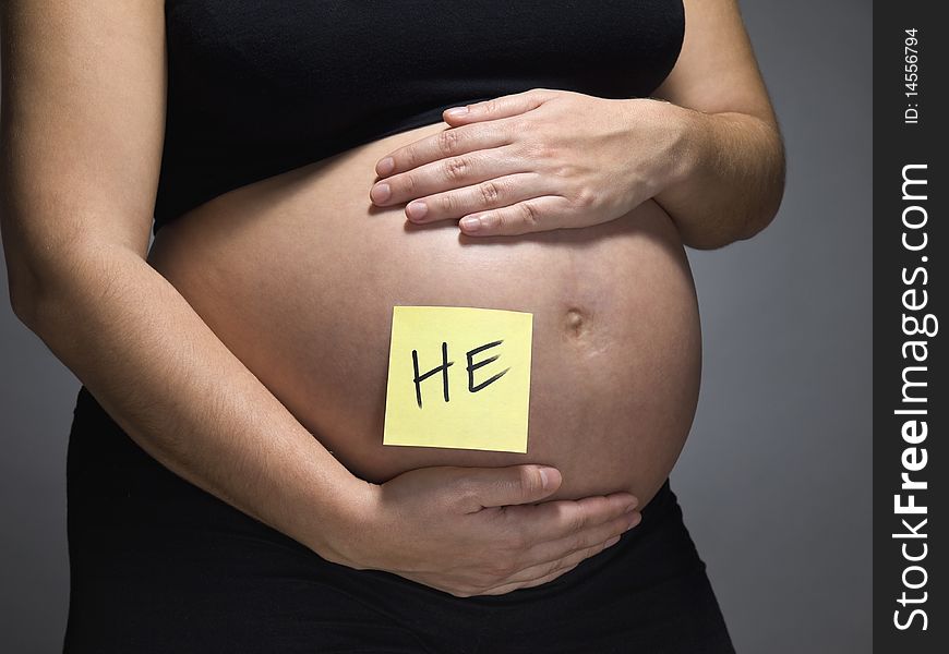 Pregnant woman with a sticky note saying HE on her belly. Pregnant woman with a sticky note saying HE on her belly.