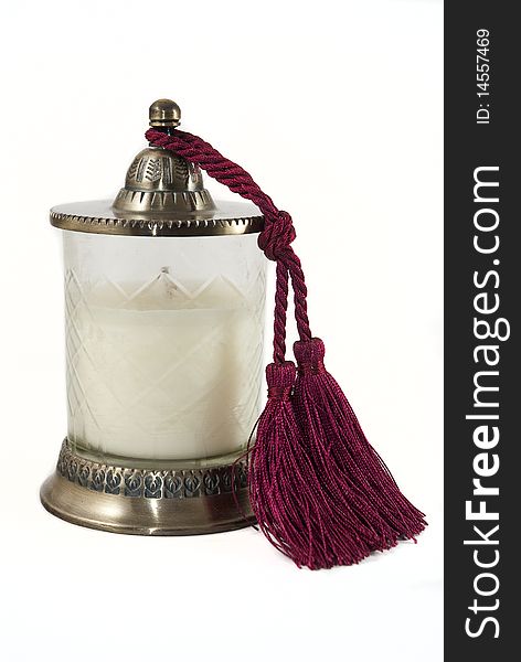 White candle in holder with wine-red tussle hanging on the side. White candle in holder with wine-red tussle hanging on the side