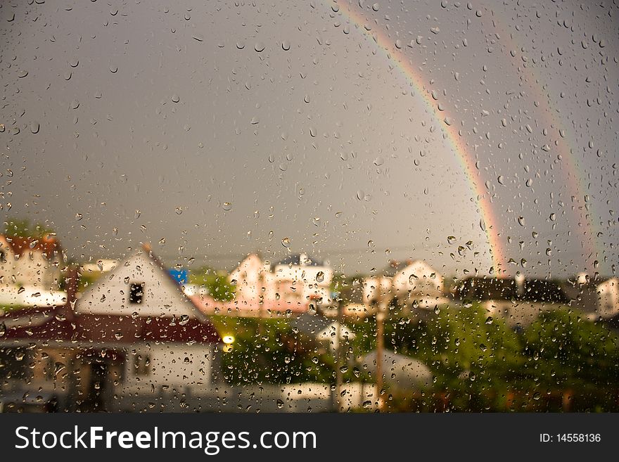 This is a picture of droplets on the glass on the background of the rainbow and houses. This is a picture of droplets on the glass on the background of the rainbow and houses