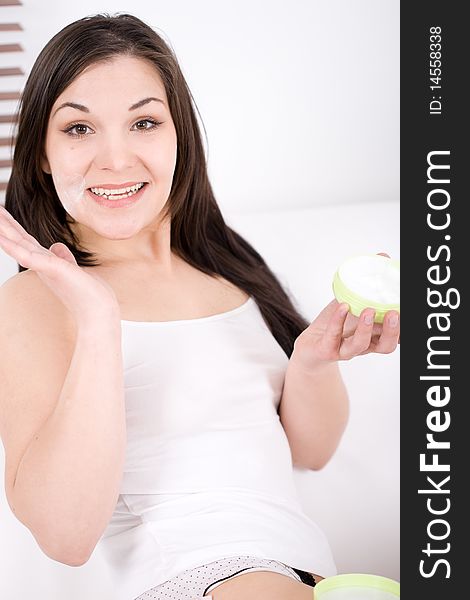 Young brunette woman applying cream in bed