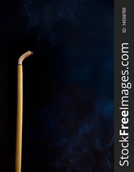 Burning solitary incense stick on a dark smoky background