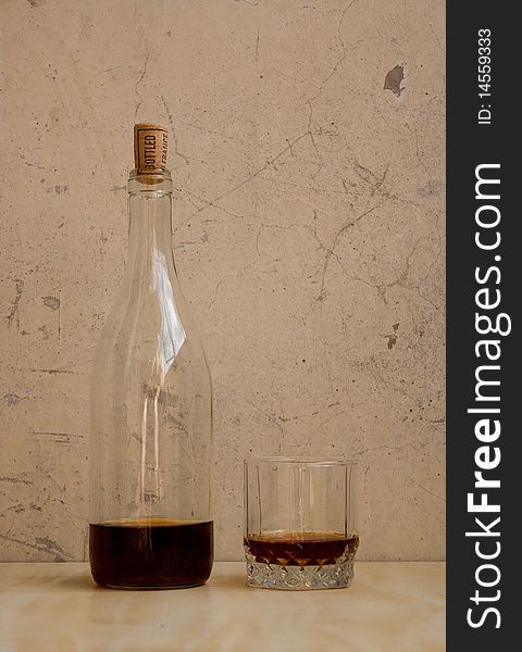 Bottle and glass stand against the wall. It have a drink. Bottle and glass stand against the wall. It have a drink.