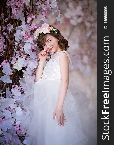 A girl in a long white dress against a garland of white and pink flowers. Studio shooting