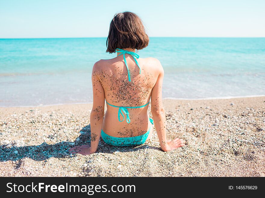 Girl on the beach with sand on his back looks at the ocean. fun on holidays in the sand