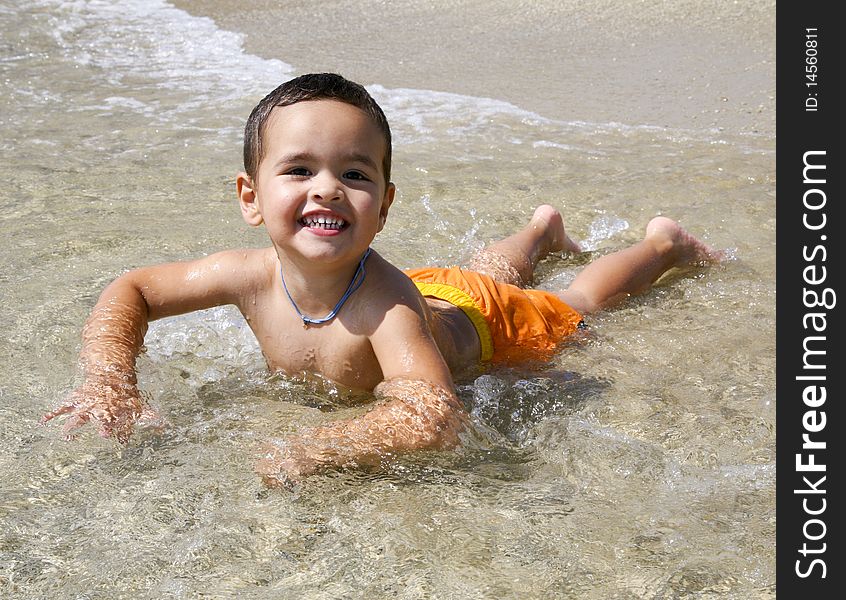 A smiling three year old Greek boy in orange swimsuit playing in the surf. A smiling three year old Greek boy in orange swimsuit playing in the surf.